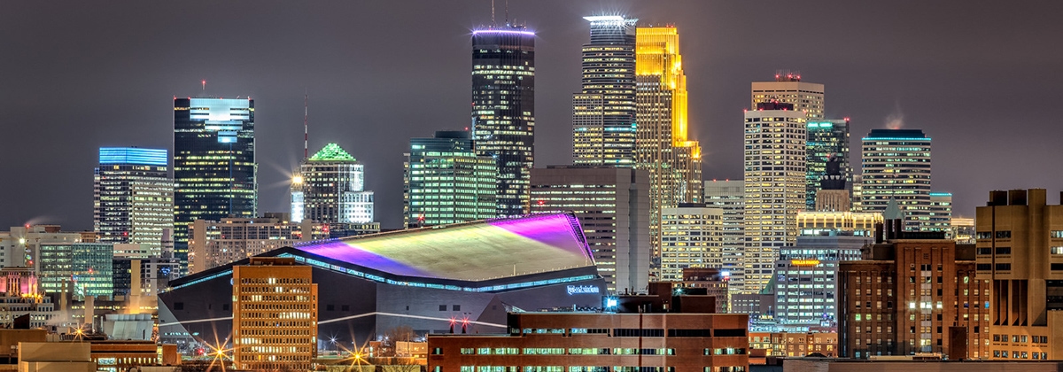 Nighttime view of downtown Minneapolis skyline with illuminated buildings and a prominent sports stadium, highlighting top Super Bowl activities.