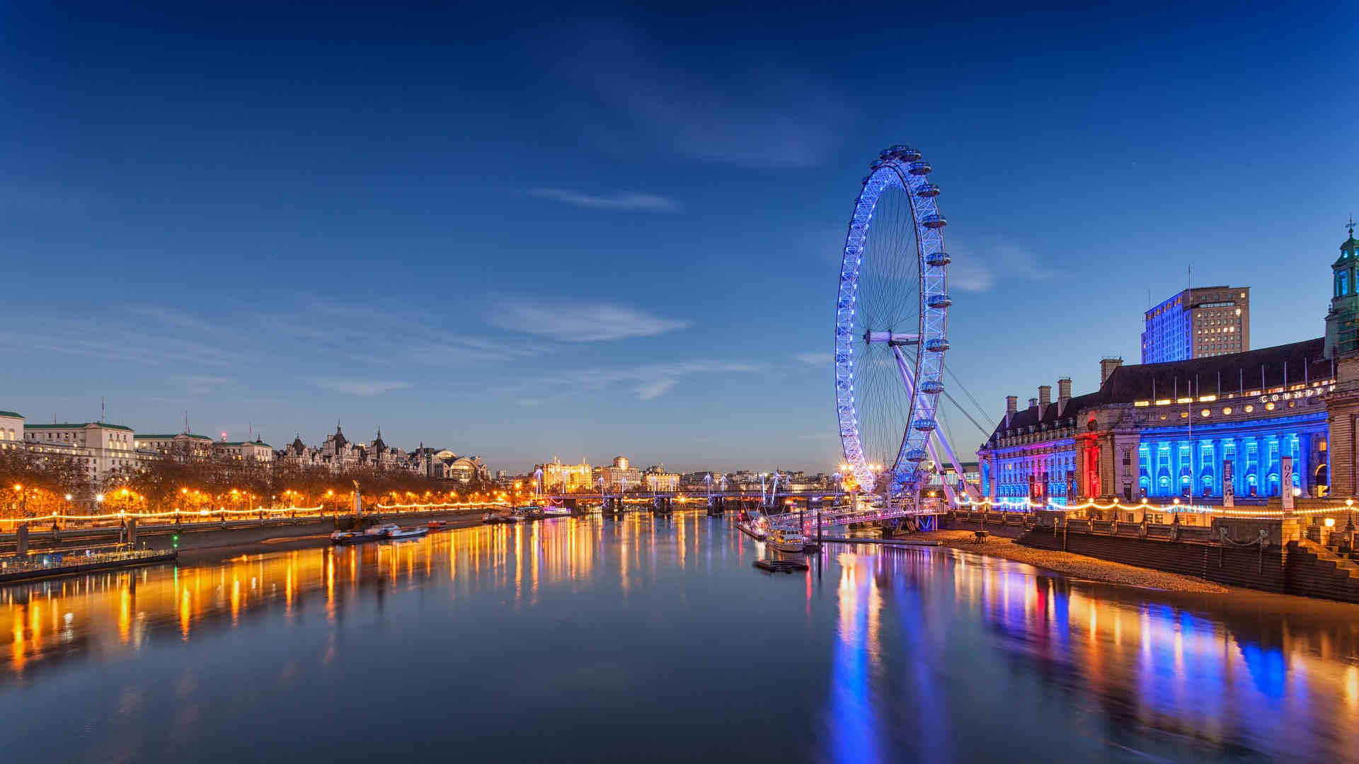 Twilight view of the illuminated London Eye beside the River Thames, reflecting cultural and entertainment aspects during the Wimbledon season.