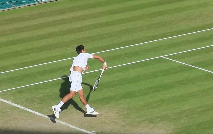 Tennis player in action on the green grass courts at the Wimbledon Championships, showcasing a dynamic match moment, ideal for luxury travel and tour packages in London.