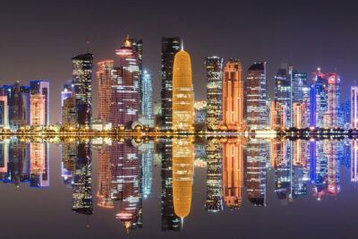 Nighttime view of Doha's illuminated skyline reflected in water, highlighting popular destinations during the World Cup in Doha.