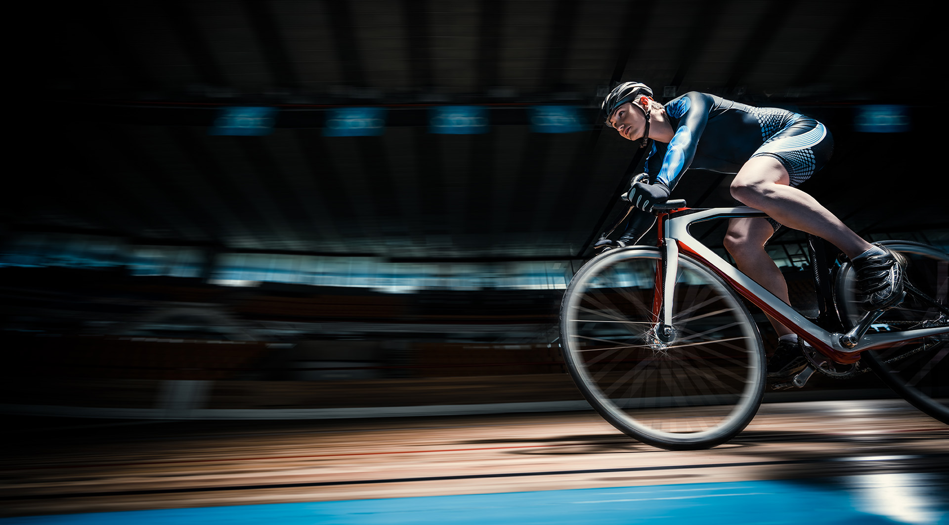 A cyclist in a blue and white suit speeds around a velodrome, captured in motion blur, highlighting the excitement of sports travel experiences.