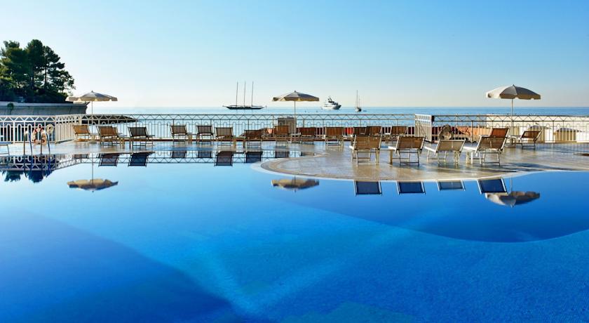 Luxury Monaco Grand Prix Hotel at Le Meridien Beach Plaza showcases an inviting swimming pool overlooking the sea, lined with sun loungers under parasols, perfect Grand Prix accommodations in Monte Carlo.
