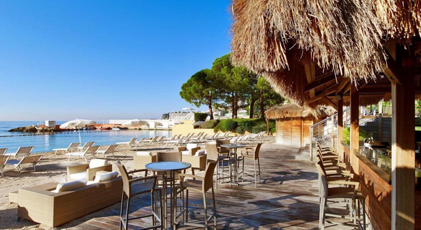 Outdoor seating at Le Meridien Beach Plaza in Monaco overlooks a serene beach, ideal for discerning guests seeking Monaco Grand Prix Hotels & Accommodations.