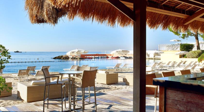 View from an outdoor terrace at Le Meridien Beach Plaza in Monte Carlo, featuring beach loungers, thatched sun umbrellas, and a calm sea, making it ideal for Monaco Grand Prix accommodations.