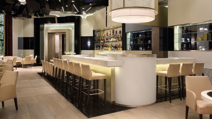 Elegant bar area inside the Excelsior Hotel Gallia, featuring a white bar counter, cream stools, and chic lighting, perfect for guests attending the Italian Grand Prix in Milan.