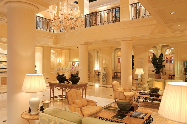 Elegant lobby of a luxury hotel in Monaco, showcasing plush seating, grand columns, and a striking chandelier, ideal for Monaco Grand Prix accommodations.