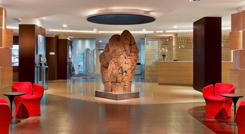 Sleek, modern hotel lobby with red chairs and an abstract sculpture, depicting luxury accommodations for the Monaco Grand Prix at Le Meridien Beach Plaza, Monte Carlo.
