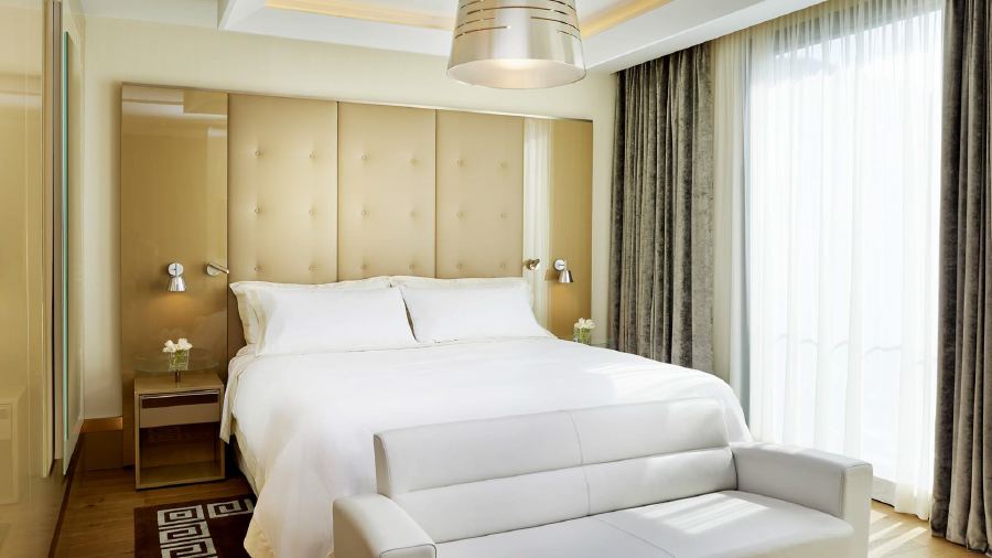 Elegant hotel room featuring a plush white bed, modern furniture, and large windows, ideal for visitors looking for luxury accommodations at the Italian Grand Prix in Milan.