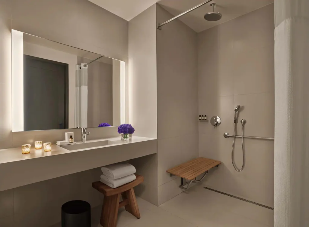 Luxurious ADA-compliant loft bathroom in New York featuring neutral tones, accessible shower with bench, and elegantly lit mirror, ideal for Ryder Cup accommodations.