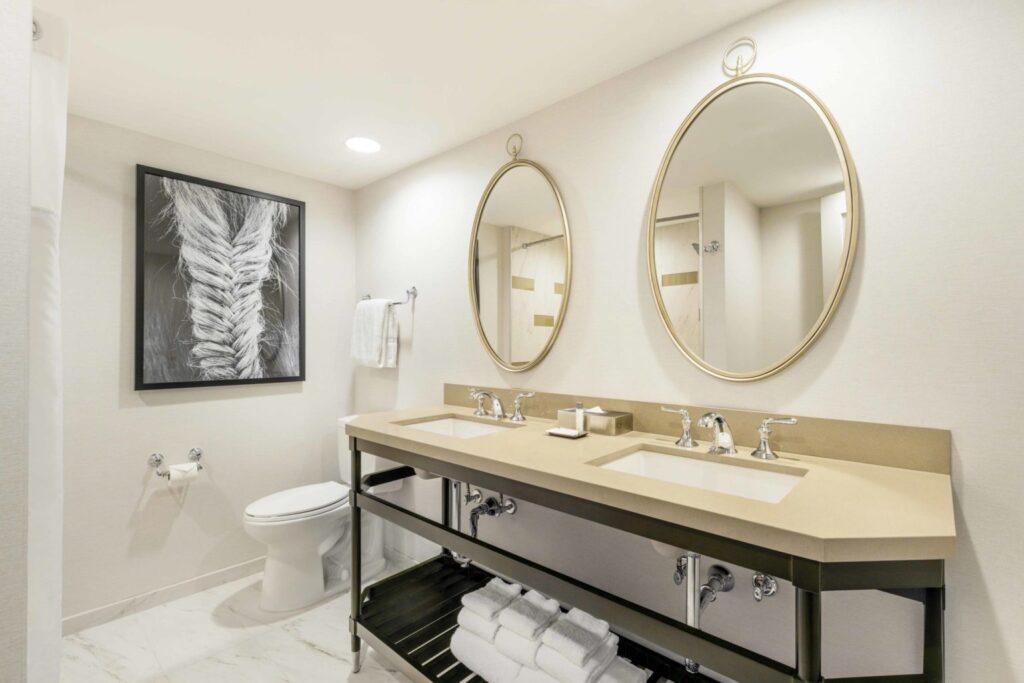 Elegant double-sink bathroom in a Louisville hotel near Churchill Downs, featuring oval mirrors, clean lines, and sophisticated decor, ideal for Kentucky Derby accommodations.