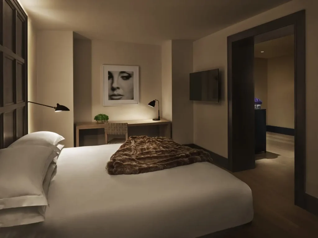 Luxurious hotel bedroom at The New York EDITION featuring elegant decor, subdued lighting, and a framed portrait, ideal for guests attending the Ryder Cup in New York.