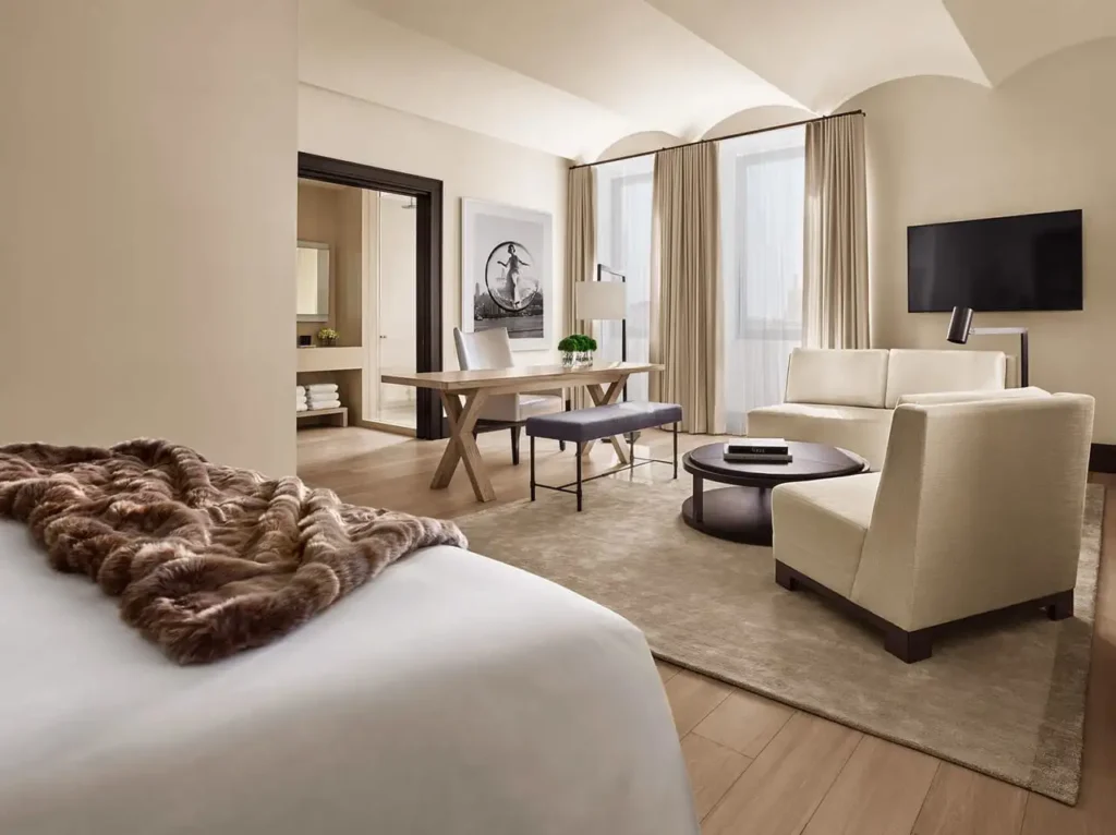 Luxurious hotel suite in New York featuring a stylish living area with beige sofas, a workspace, and modern art, ideal for accommodations near the Ryder Cup events.