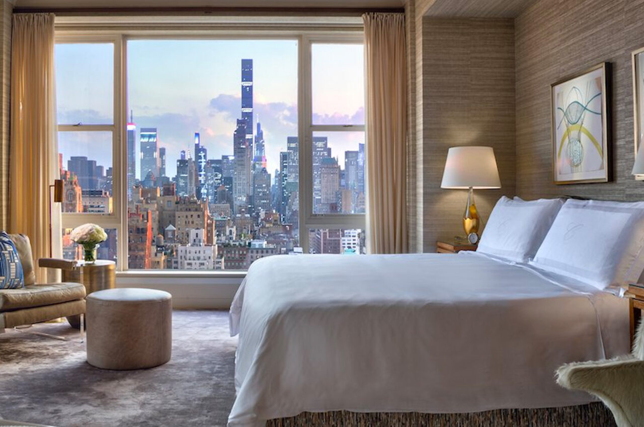 A luxurious hotel room with a large bed, elegant furniture, and an expansive view of the New York City skyline from the window, ideal for World Cup accommodations.