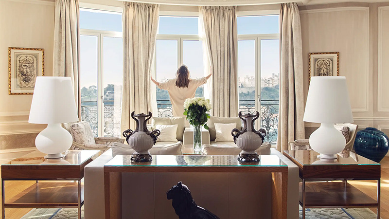 A woman stands at the window in a luxuriously appointed room at the Hotel Hermitage in Monaco, overlooking scenic views, ideal for experiencing Monaco Grand Prix hotel packages.