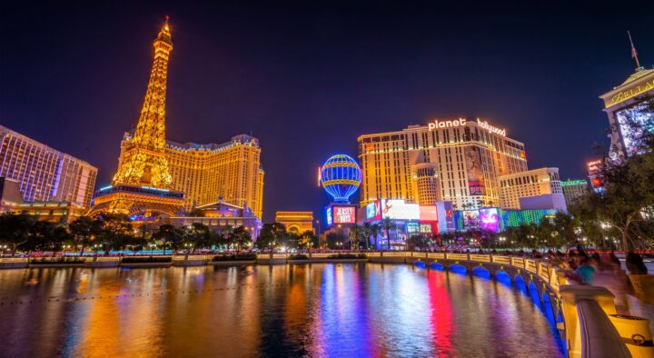Night view of the Las Vegas strip showcasing illuminated hotels and a reflection over a water body, highlighting popular tourist destinations and roadtrips in the Las Vegas area.