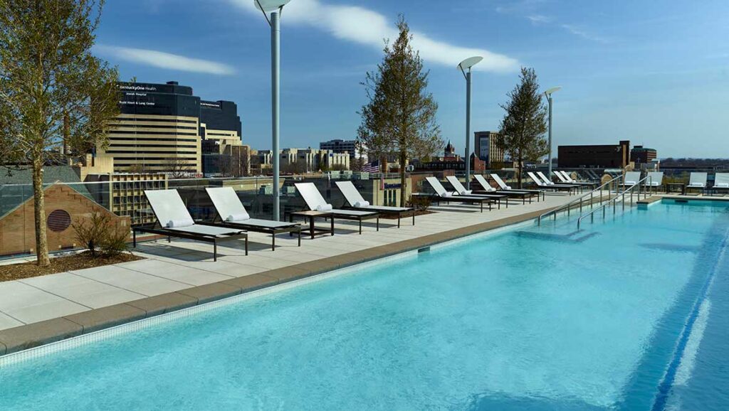 Outdoor rooftop pool at Omni Louisville, featuring aligned lounge chairs and a view of the cityscape, ideal for visitors looking for luxury accommodations near Churchill Downs for the Kentucky Derby.