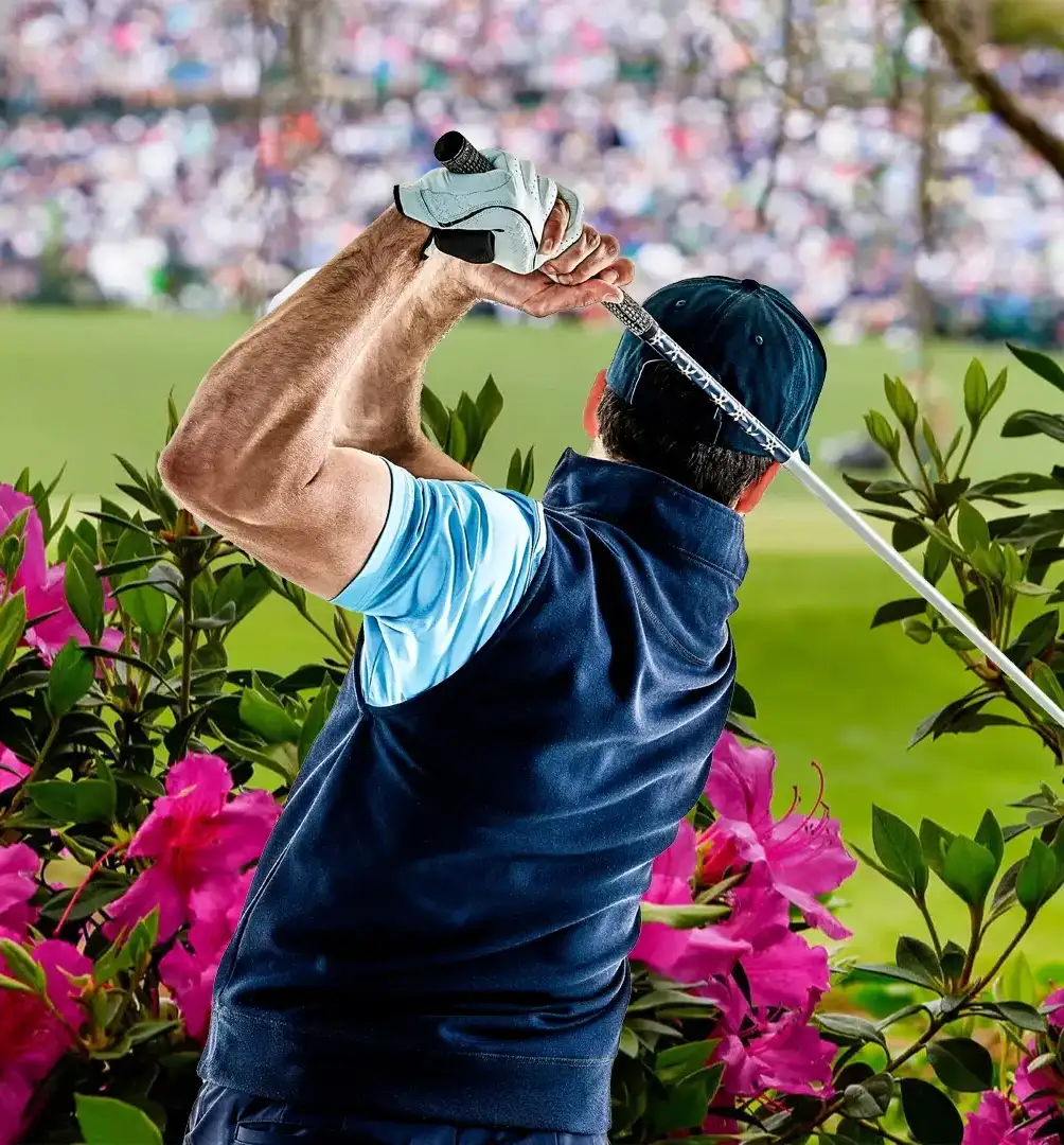 A golfer at Augusta National Golf Club adjusts his cap, surrounded by vibrant flowers, with a blurred crowd of spectators in the background.