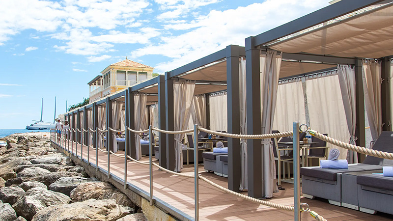 Luxurious cabanas line a seaside walkway at the Monte Carlo Bay Hotel in Monaco, ideal for accommodations during the Monaco Grand Prix, featuring plush seating and ocean views.