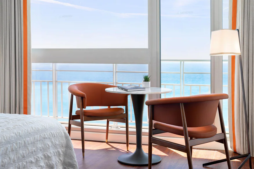 Deluxe guestroom at Le Meridien Nice, featuring a comfortable seating area and balcony overlooking the ocean, ideal for Monaco Grand Prix accommodations.