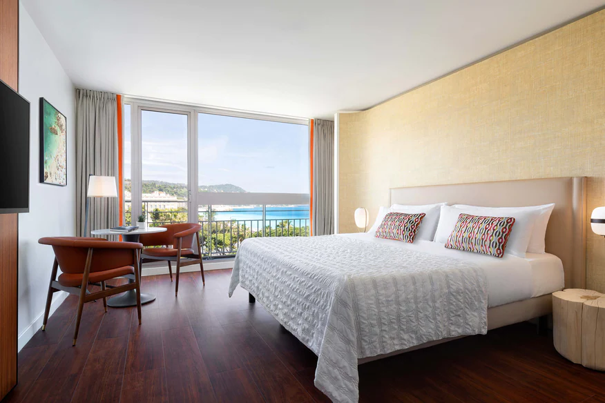 Spacious guest room at Le Meridien Nice features a comfortable bed, modern furnishings, and a balcony overlooking the ocean, ideal for the Monaco Grand Prix.