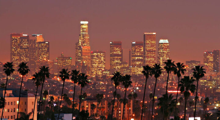 Palm trees silhouette against the glittering skyline of downtown Los Angeles during twilight, showcasing the vibrant urban life near the Rose Bowl in Pasadena.