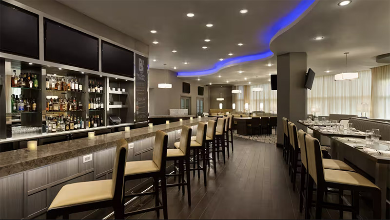 Modern hotel bar and dining area featuring a well-stocked bar, high stools, and ambient blue lighting, located at The Park Hotel at Meadowlands, a recommended accommodation for World Cup travelers.