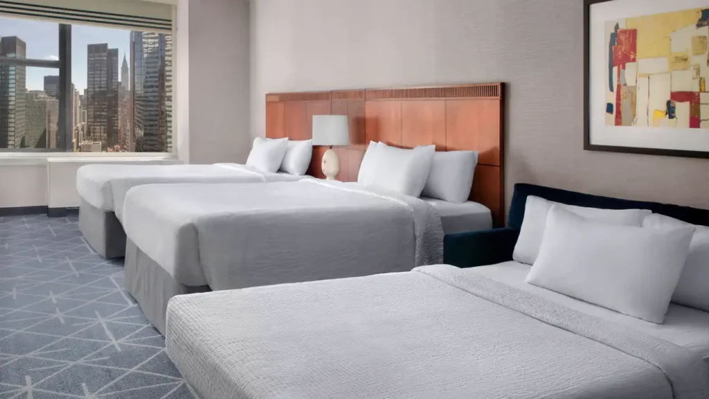 This luxurious hotel room features two queen-sized beds, stylish decor, and large windows offering a stunning view of the New York city skyline, ideal for guests attending the US Open Tennis event.