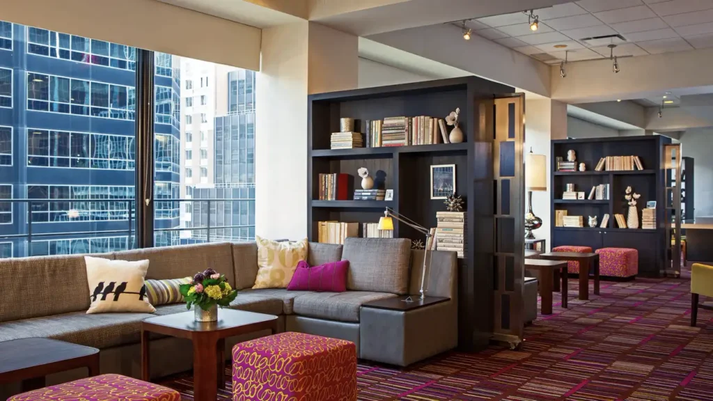 View of a stylish lobby area at the Courtyard Midtown East on Third Avenue, New York, featuring comfortable seating, bookshelves, and large windows with city views, near US Open Tennis accommodations.
