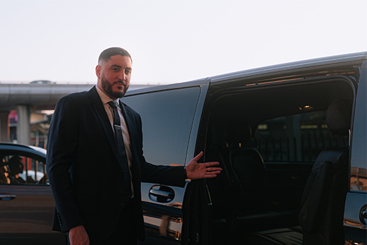 A man in a suit welcomes passengers to a private transfer vehicle, commonly used for luxury travel and tours at major events in Milan and Cortina.