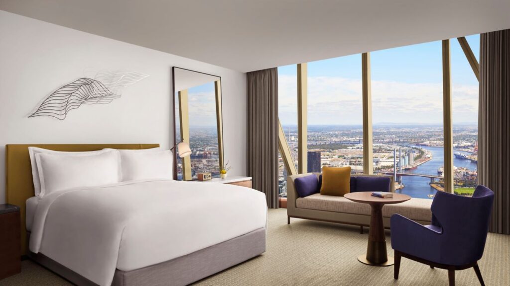 Luxurious hotel room at The Ritz-Carlton Melbourne on Lonsdale Street, featuring a sleek design with a large bed, modern furniture, and expansive windows that offer a panoramic view of the Melbourne skyline and waterfront. Ideal for visitors attending Australian Open events at Melbourne Park.