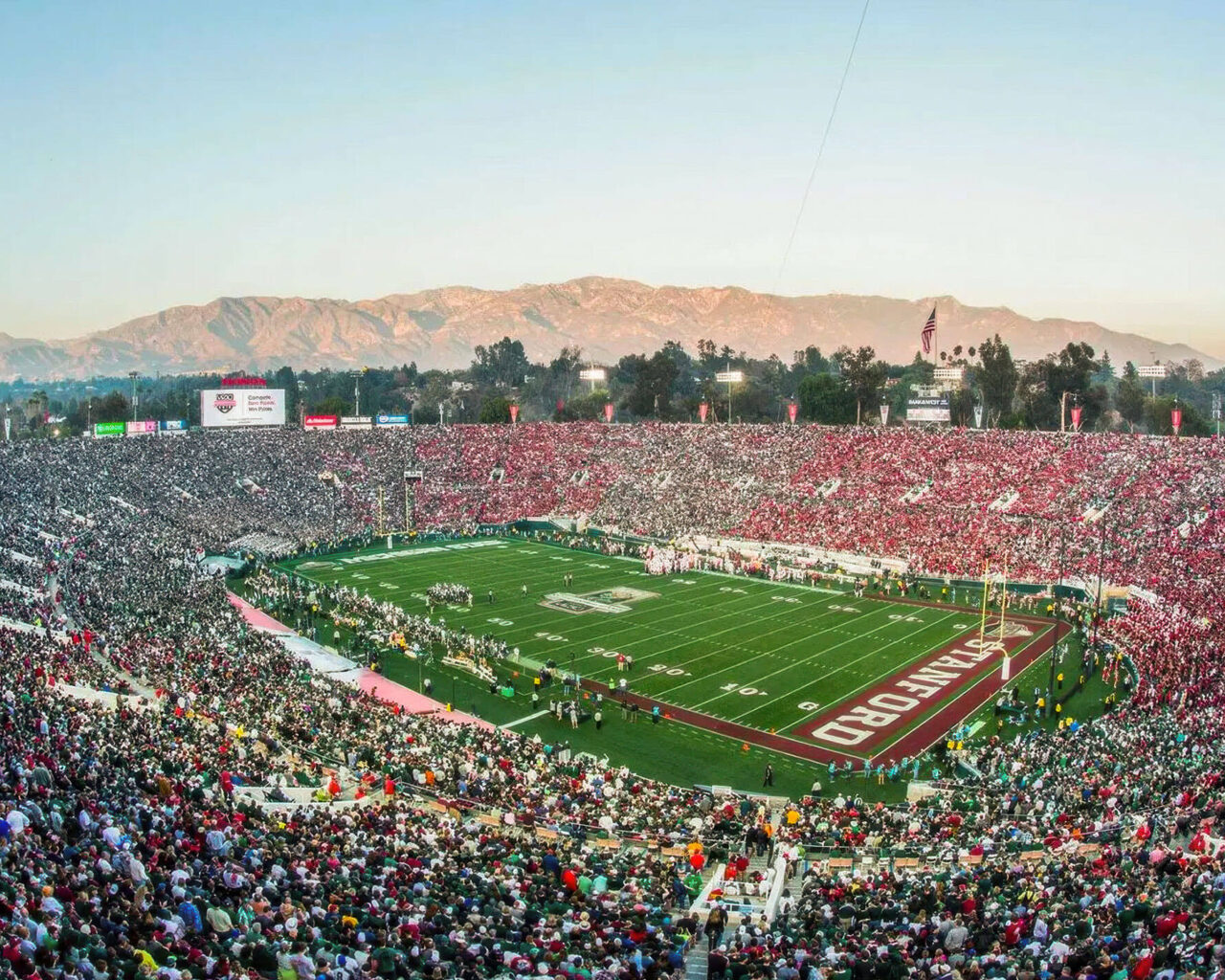 A panoramic view of a packed stadium during a football game, set against a backdrop of mountains, ideal for those seeking football travel packages that include hotel and ticket options.