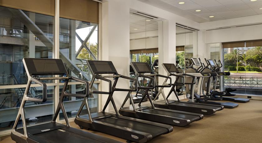 Row of treadmills in a modern gym with large windows, located in Hotel Arts Marina, Barcelona.
