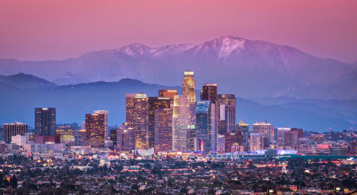 Downtown Los Angeles skyline during sunset with illuminated buildings and distant mountains, providing a backdrop for the Summer Games Los Angeles Area Map.