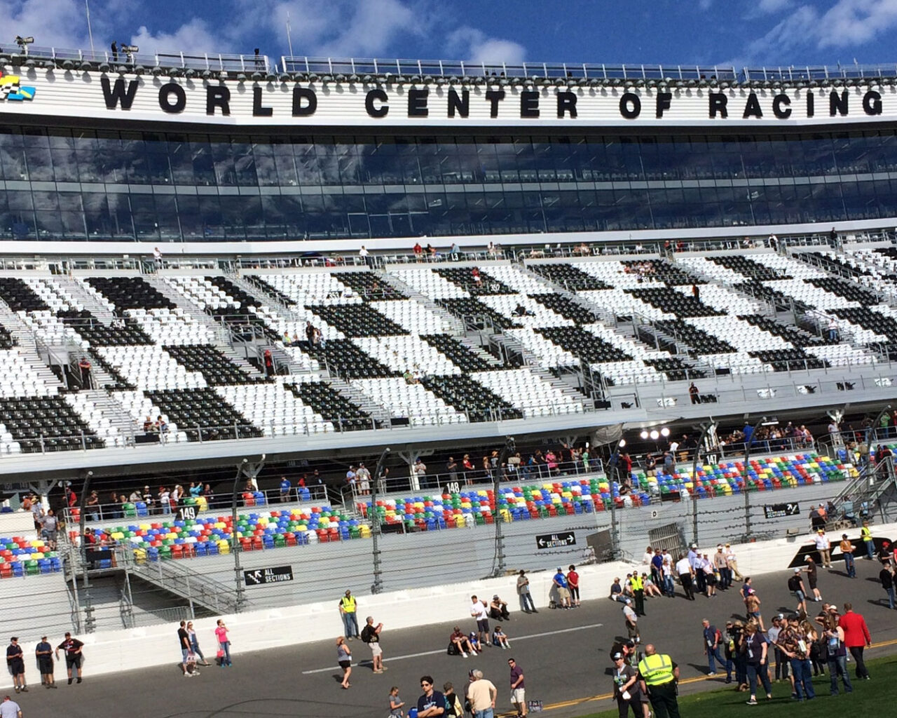 View of the Daytona International Speedway, showing crowded stands and spectators on the track, with the 'WORLD CENTER OF RACING' signage displayed prominently above.