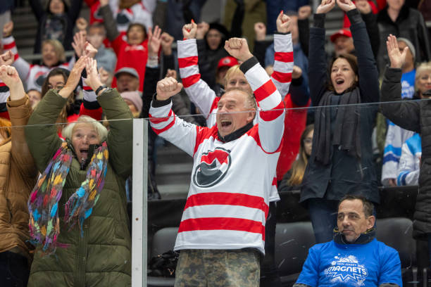 Hockey fans cheer excitedly at a game, featuring one man in a striped jersey raising his arms in victory, enhancing the atmosphere for those seeking Stanley Cup Final travel packages.
