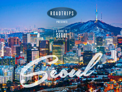 Nighttime view of Seoul with illuminated skyscrapers and Namsan Seoul Tower in the background, promoting a luxury travel guide by Roadtrips.