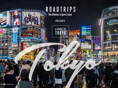 Crowded street scene at night in Tokyo with illuminated advertisements and a large 'Tokyo' text overlay, as part of a luxury travel guide by Roadtrips.
