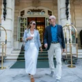 A mature couple happily exits a luxury hotel, engaging in conversation, representing a high-end sports travel package experience.